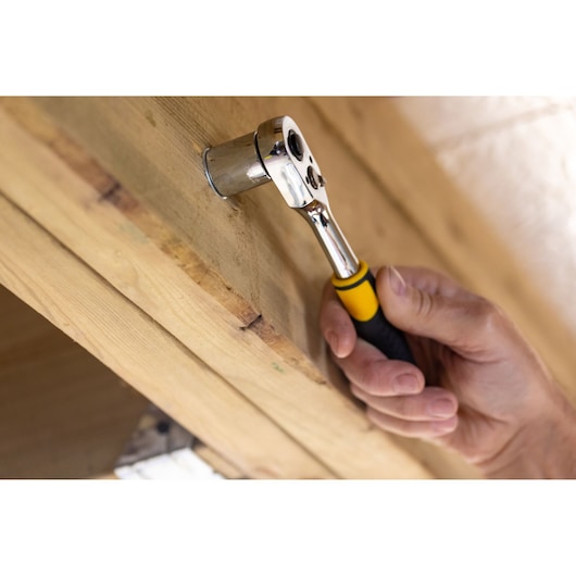 STANLEY STMT82671-0 ratchet wrench with yellow handle tightening bolt on wood surface, close-up photo.