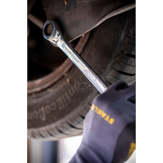 Photo of STANLEY STMT82842-0 combination wrench in use on a car tire bolt, held by a gloved hand.