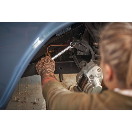 STANLEY STMT82846-0 flat ratcheting wrench used on car brake line, mechanic's tattooed arm visible.