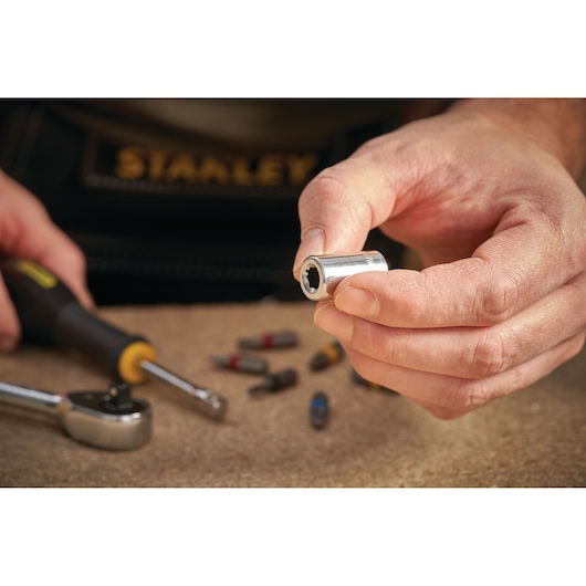 Photo of STANLEY STMT86124-0 socket held in hand, with ratchet and bits on workbench.
