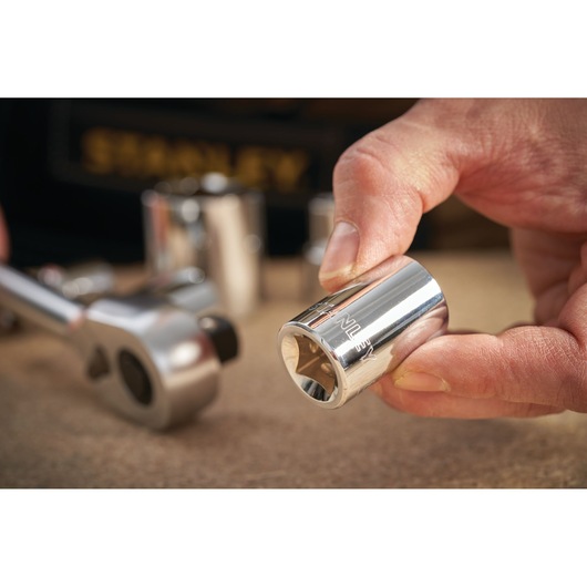 Photo of STANLEY STMT86517-0 chrome socket held by hand, with ratchet and other sockets in background.