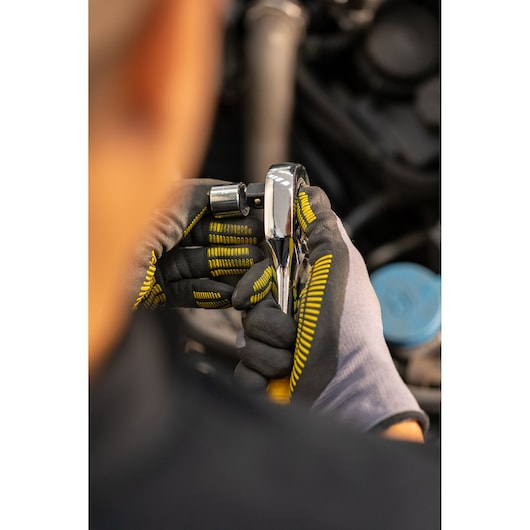STANLEY STMT86527-0 ratchet tool held by gloved hands, close-up, in workshop setting.