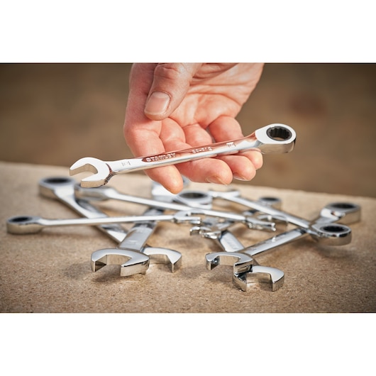 STANLEY STMT89912-0 combination ratcheting wrench held in hand, with other wrenches on a workbench.