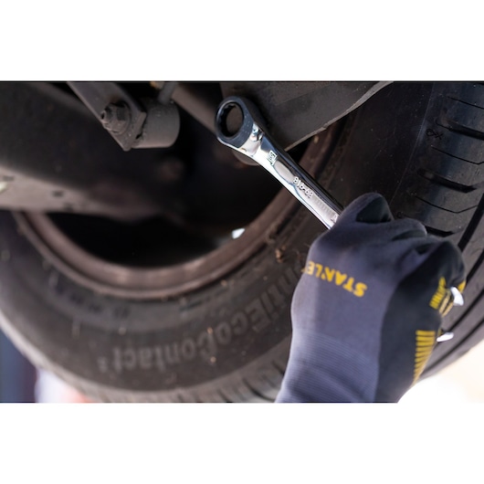 Photo of STANLEY STMT89917-0 ratcheting wrench used on car wheel, gloved hand visible, automotive context.