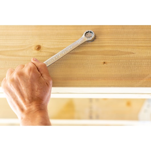 Photo of a hand using STANLEY STMT95908-0 ratcheting wrench on a wood beam, close-up side angle.