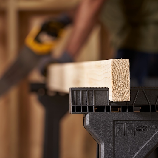 STANLEY STST1-70355 sawhorse holding wood beam, close-up in workshop setting.
