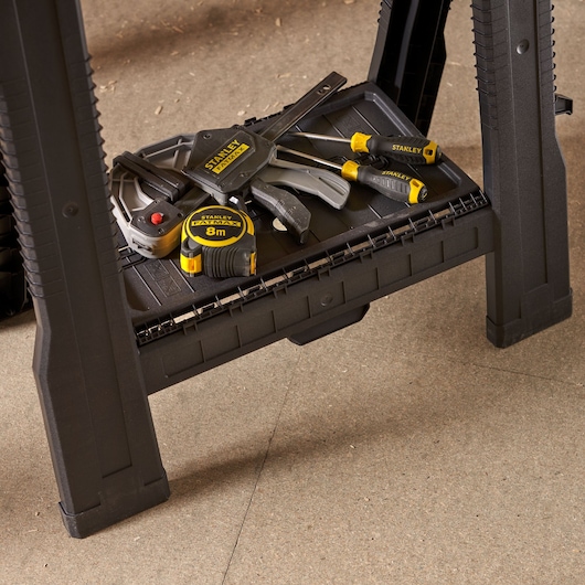 STANLEY STST1-70355 workbench lower shelf with assorted STANLEY hand tools, tape measure, screwdrivers, and clamps.