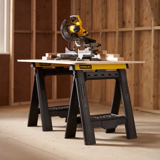 Stanley STST1-70559 black and yellow sawhorses used as a workbench in a construction setting, side angle.
