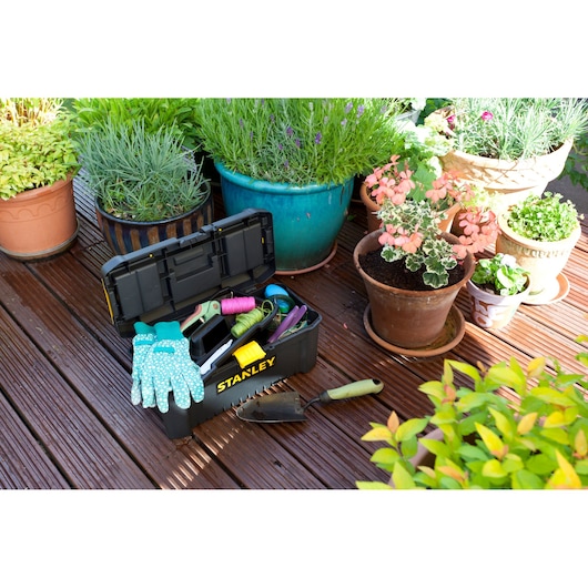 Stanley STST1-75517 toolbox with gardening tools and gloves on wooden deck near potted plants, outdoor angle.