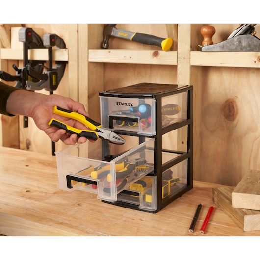 STANLEY STST40711-1 three-drawer tool organizer, photo in workshop setting with hand holding pliers.