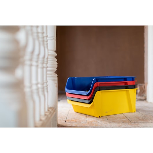 STANLEY STST70348-1 stackable plastic storage bins in yellow, black, red, and blue on wooden floor, side view.