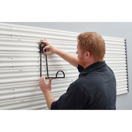 Photo of STANLEY STST82614-1 wall storage hook being mounted on white slatwall panel, side angle.
