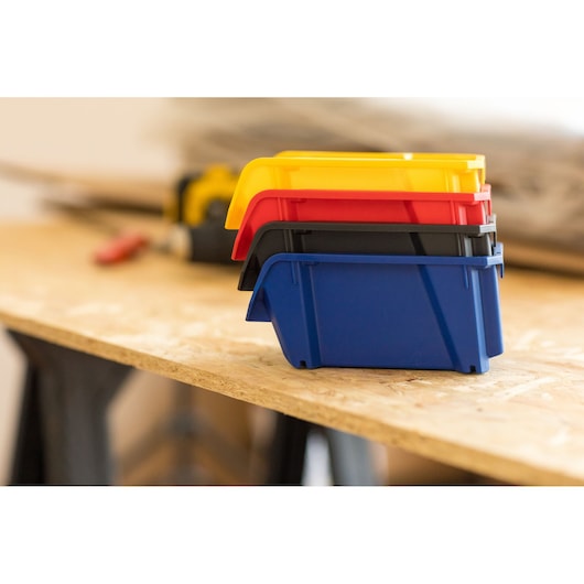 STANLEY STST82710-1 stackable storage bins in yellow, red, black, and blue on a workshop table, side angle.