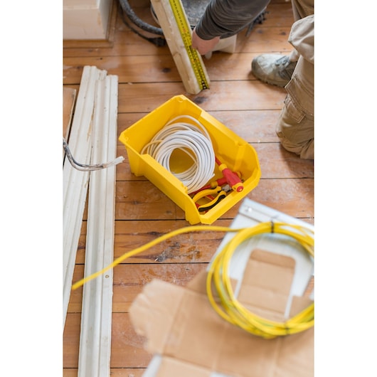 STANLEY STST82714-1 yellow storage bin holding coiled cables and tools on a wooden floor at a worksite.