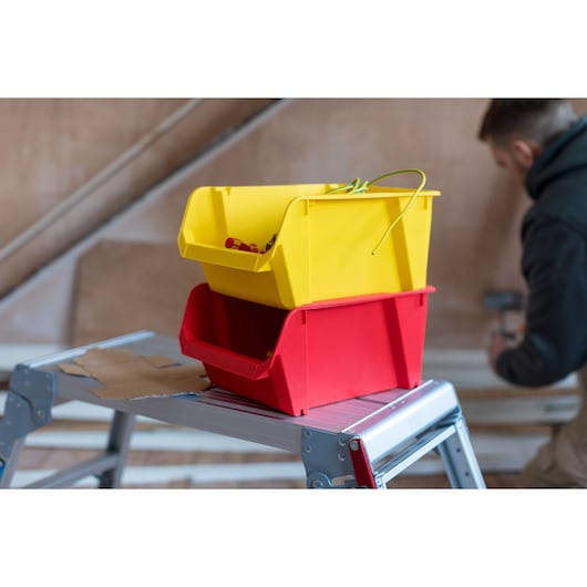 STANLEY STST82714-1 stackable yellow and red storage bins on step ladder, workshop setting.