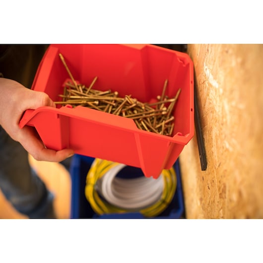STANLEY STST82739-1 red storage bin holding metal screws, close-up angle, on workshop wall.