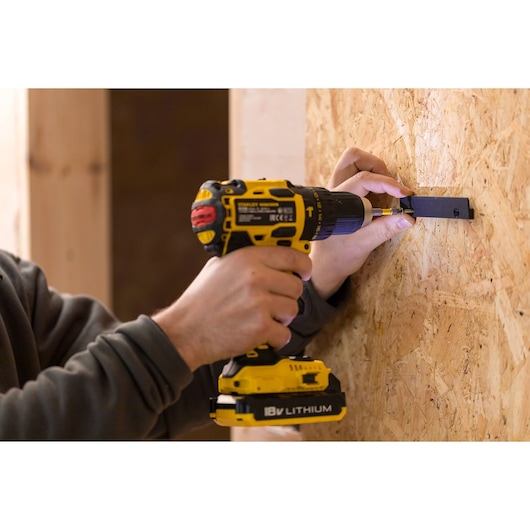STANLEY STST82964-1 cordless drill in use on wood wall, side angle, yellow and black.