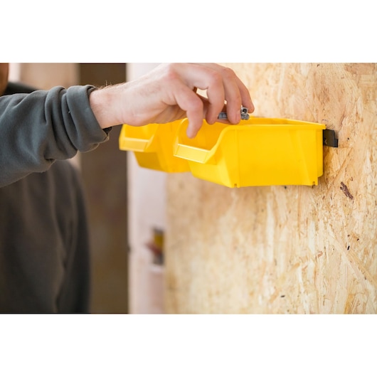 STANLEY STST82964-1 yellow storage bins mounted on wall, hand placing hardware, photography close-up.