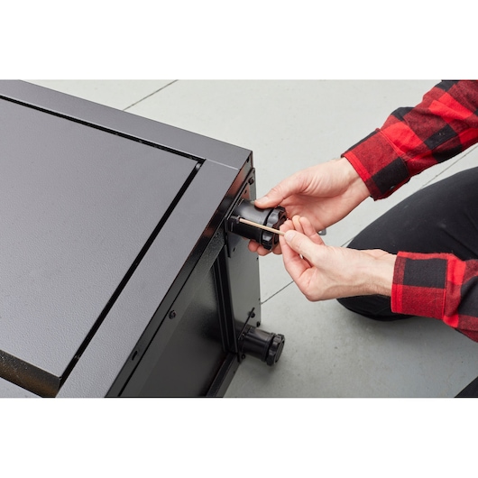 STANLEY STST97957-1 photography of a person assembling caster on black metal cabinet.