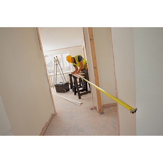 STANLEY XTHT0-33503 tape measure used by worker in construction setting, extended across doorway.