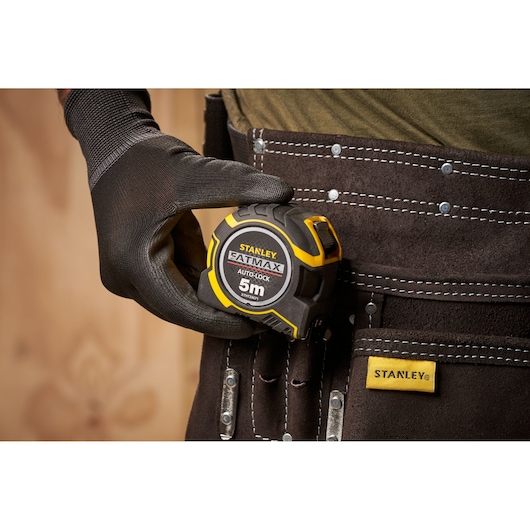 STANLEY XTHT0-33671 tape measure held by gloved hand, shown clipped to tool belt, close-up view.
