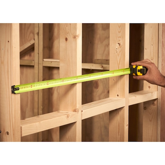 STANLEY XTHT0-36004 tape measure extended across wooden studs, side angle, used for construction measurements.