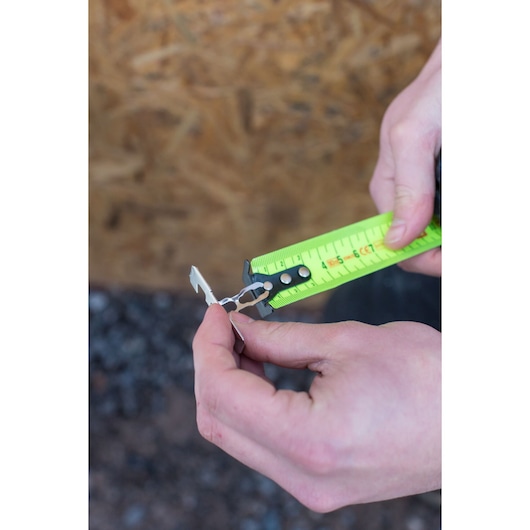 Photo of STANLEY XTHT0-36004 tape measure with green blade in use, close-up of hands outdoors.