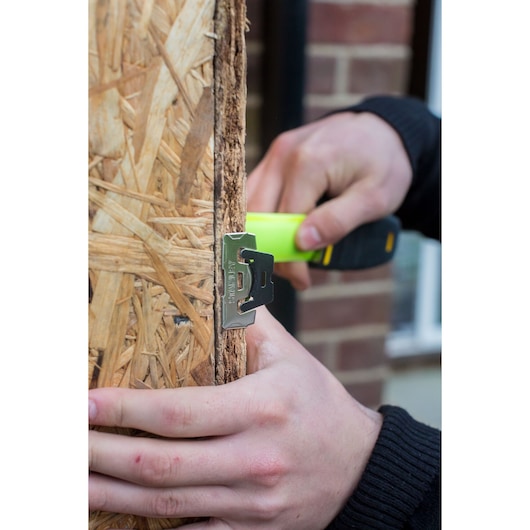 STANLEY XTHT0-36004 photography showing hand using green and black tool on wood edge outdoors.