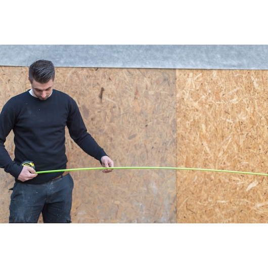 STANLEY XTHT0-36005 measuring tape held by person against wooden panel wall.