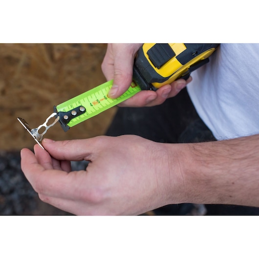 STANLEY XTHT0-36005 tape measure with bright yellow blade held in hand measuring small metal bracket.