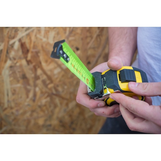 Photo of STANLEY XTHT0-36005 tape measure with green blade being held by hands, used for measuring wood.