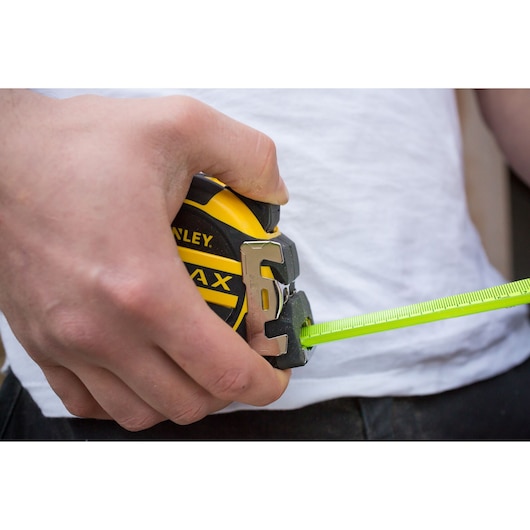 Photo of STANLEY XTHT0-36005 tape measure in hand, bright yellow and black case, extended green blade.