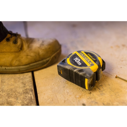 STANLEY XTHT0-36005 tape measure FATMAX 10m on dusty workshop floor near boot and screw.