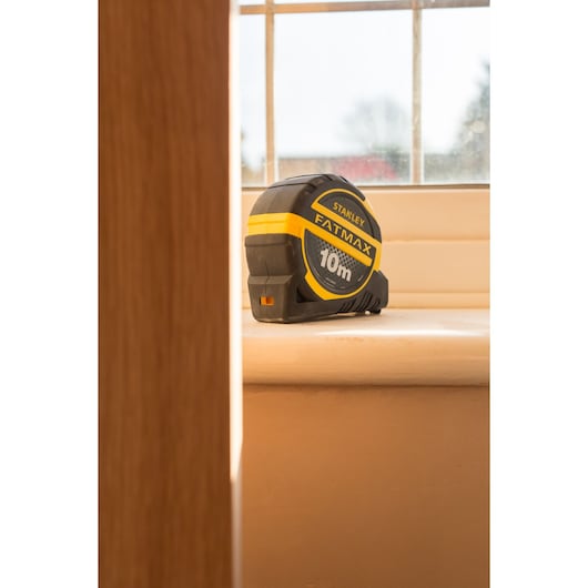 STANLEY XTHT0-36005 tape measure FATMAX 10m, black and yellow, side angle on windowsill.