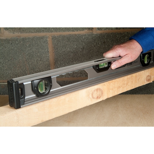 Stanley XTHT1-42131 spirit level held on wood beam, construction context, side angle.